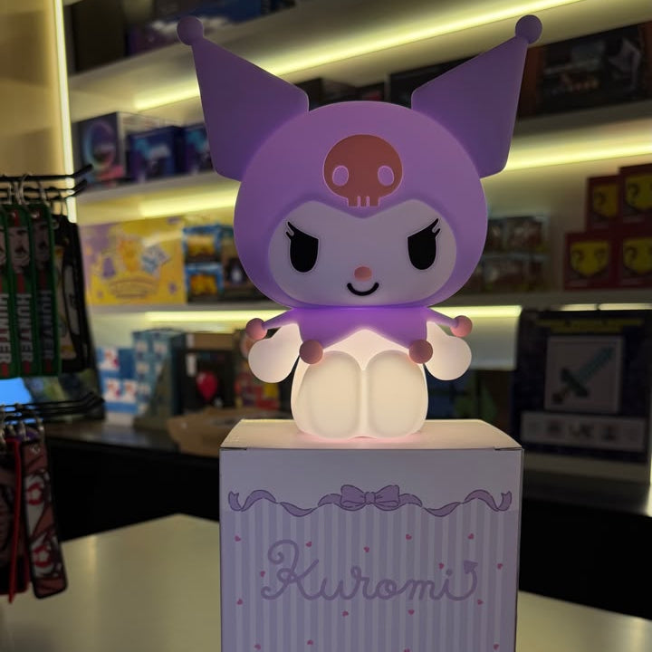 A Kuromi collectible figure with a glowing white body and purple ears, displayed on top of its branded purple box in a retail store setting.