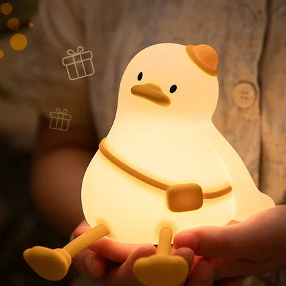 Chick-shaped night light held in a hand with a warm glow against a blurred background.