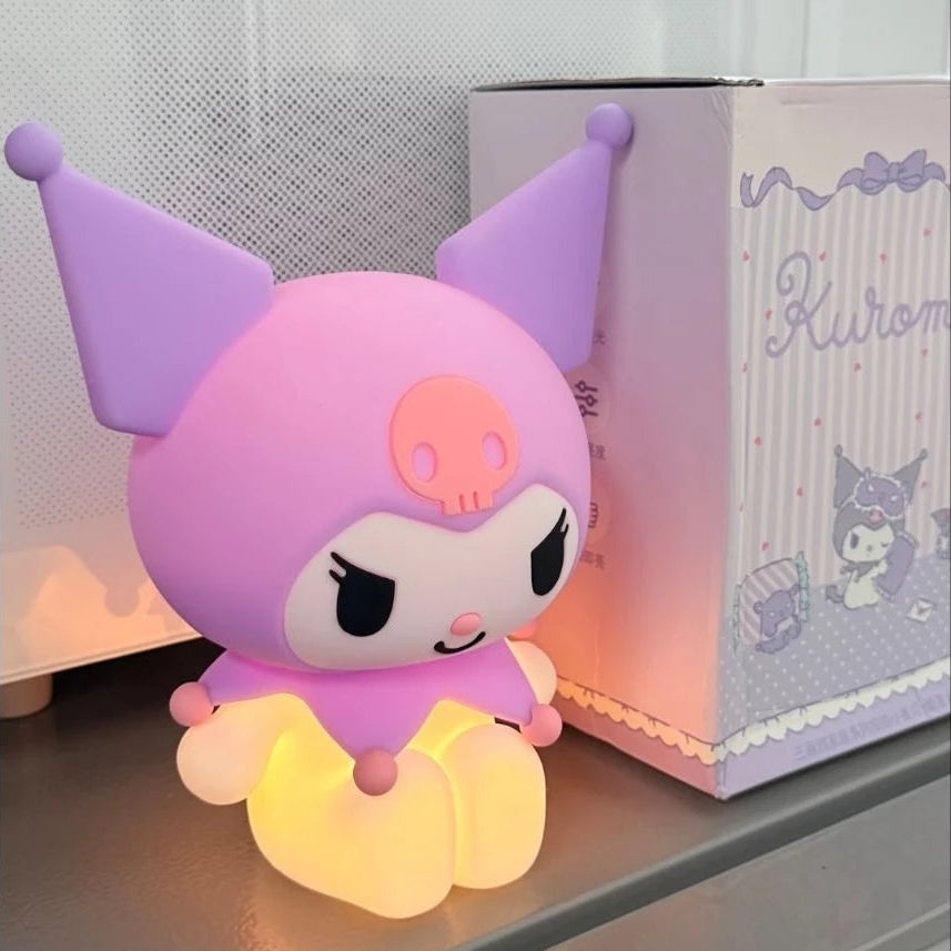A Kuromi character night light glowing with warm yellow light, positioned next to its decorative product box on a shelf.