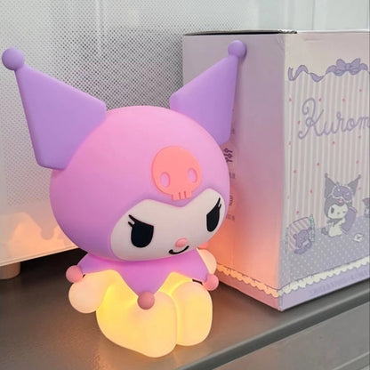 A Kuromi character night light glowing with warm yellow light, positioned next to its decorative product box on a shelf.